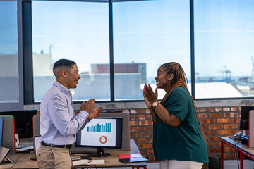 Diverse coworkers celebrating success at modern office desk, computer monitor and red folder
