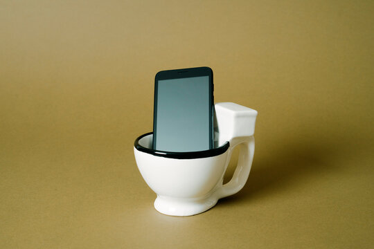 Smartphone in ceramic toilet representing digital detox in a minimalist studio