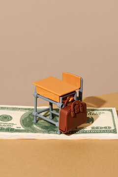 Miniature school desk and bag on dollar bill symbolizing education cost