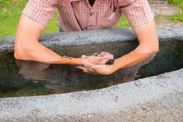 Man immerses both arms in ice-cold water. Stone trough, Kneipp pool for arms.