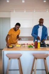 Selbstklebende Fototapeten Zu Kochen African american father, son cooking meal at kitchen island chopping vegetables on cutting board  © wavebreak3