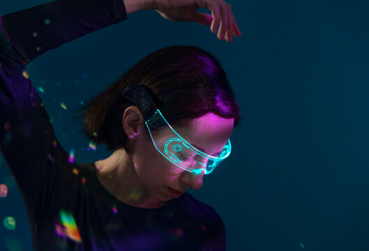 Woman with glowing virtual reality glasses indoors in futuristic light