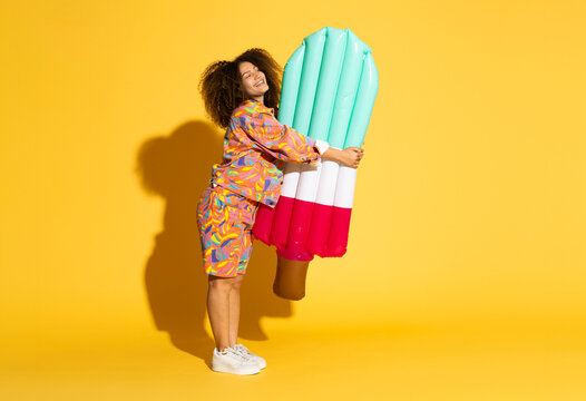 Young woman embracing pool raft against yellow background