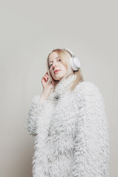 Stylish woman with fur coat and headphones listening to music