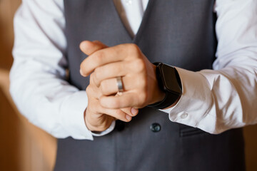 Obraz premium Elegant Groom Adjusting Wedding Ring and Smartwatch in Formal Gray Vest and White Dress Shirt