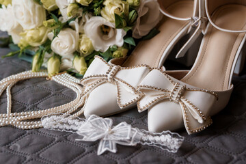Elegant White Wedding Shoes with Rhinestone Bow Accents Beside Pearl Necklace and Rose Bouquet