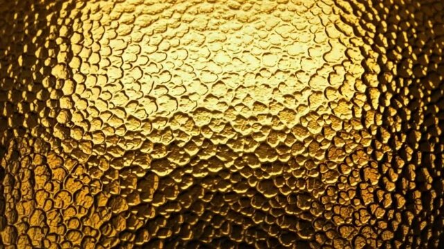 Golden textured surface with a bumpy hammered metal effect in warm lighting conditions