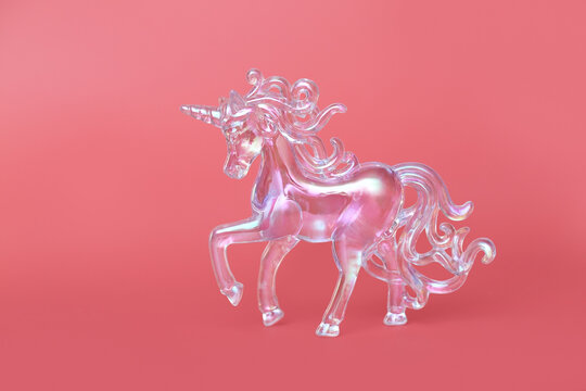 Fantasy horse made of transparent acrylic glass. A close-up of the subject. A New Year's toy. A pendant for the interior. Crystal unicorn on pink background.