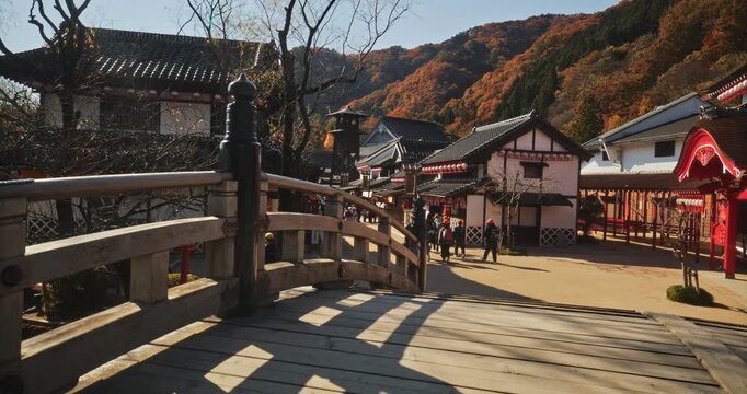 Slow motion shot across bridge in ancient Japanese village with autumn hills nearby