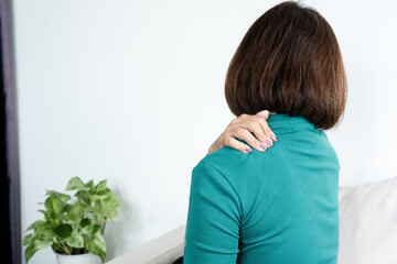 Middle-aged Asian woman suffering from shoulder pain and neck stiffness at home. Mature female touching her sore muscle, feeling exhausted from office syndrome or chronic ache