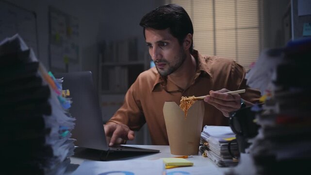 Overworked businessman facing deadline pressure while working late at night in the office, eating noodles a busy paperwork and nonstop work after hours