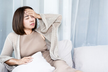 Sick middle-aged Asian woman suffering from severe headache or migraine, holding hand to forehead in pain. Exhausted mature female feeling unwell, dizzy, or stressed at home