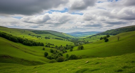 Obraz premium Lush emerald green rolling hills and deep valleys stretch toward distant mountains under a dramatic cloudy sky.