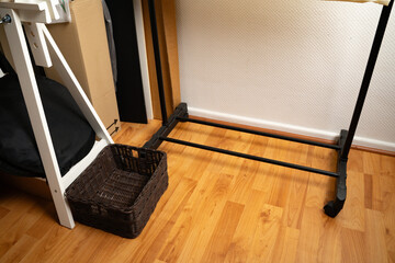 Brown woven basket placed next to wooden trestles and a shoe rack in a casual home interior. Simple storage and organization. Concept of home, interior, lifestyle, domestic, minimal.