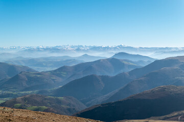 Naklejka premium A vastidão das camadas montanhosas de Iparralde sob uma névoa suave, com a cordilheira dos Pirenéus em destaque no horizonte azul em França