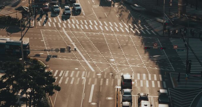 A vibrant city intersection captures the continuous movement of vehicles as they navigate crosswalks and lanes under bright sunlight. Time-lapse, Seoul, South Korea