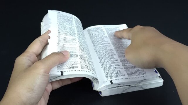 Close-up image of a woman's hand searching and looking for a word with her finger in an English dictionary, isolated on black background