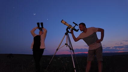 Fototapeta premium Amateur astronomers using telescope and binoculars for watching stars, Moon, planets and other celestial objests from a countryside field in nature.