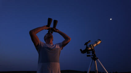 Fototapeta premium Amateur astronomer using telescope and binoculars for watching stars, Moon, planets and other celestial objects from a field in nature.