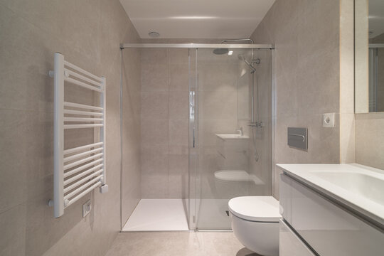 Modern bathroom with a glass shower, white toilet, and sleek sink. Neutral tile walls and a heated towel rack enhance the contemporary design.