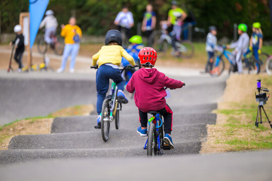 Children riding bicycles on a pumptrack in a park, wearing helmets and practicing balance and cycling skills during outdoor group activity on a sunny day.