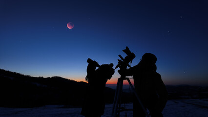 Fototapeta premium Amateur astro-photographers with a camera on a tripod photographing night sky with stars, planets, Moon eclipse and other celestial objects.