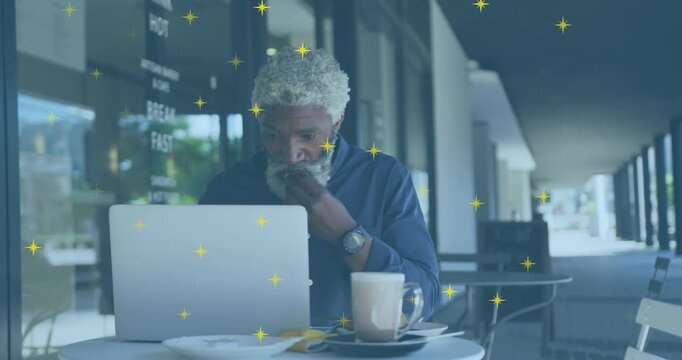 Animation of shining star icons over african american man having a snack and using laptop at a cafe