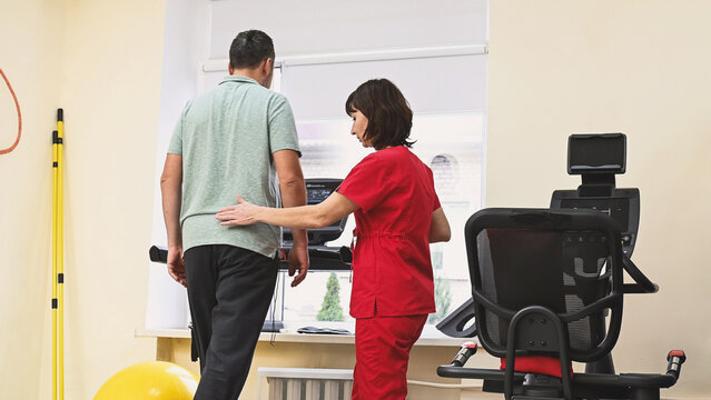 A man recovers from an injury on a treadmill under the guidance of a physical therapist. Stroke rehabilitation, physical activity.