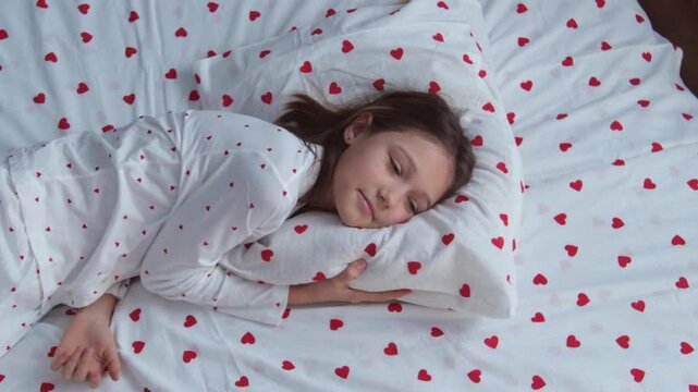 A girl in heart-patterned pajamas lies down on a pillow and falls asleep soundly.