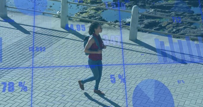 Woman walking along coastal promenade passing bollards and activating fitness charts tracking pace