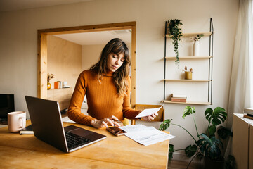 Woman managing invoices and finances at home office using laptop