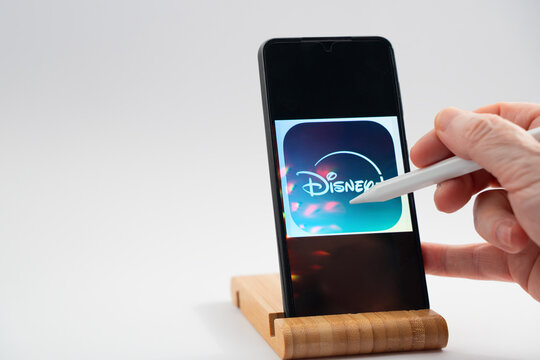 Hand using stylus on smartphone accessing disney plus streaming application