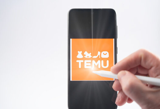 Hand interacts with the temu logo displayed on a mobile phone screen using a stylus