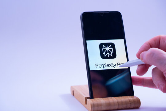 Hand engaging with perplexity pro ai app on a mobile device and wooden stand