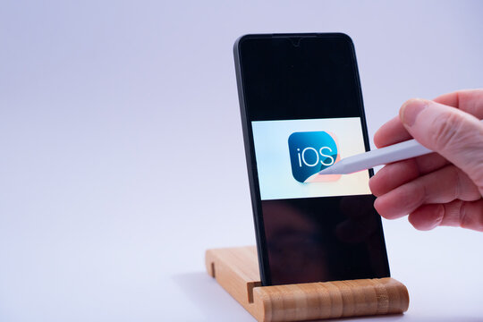 Hand interacts with a smartphone displaying the ios operating system logo using a digital stylus