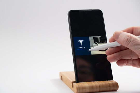 Hand using stylus on smartphone screen showing tesla logo and car