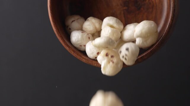 Makhana falling from wooden bowl closeup shot.