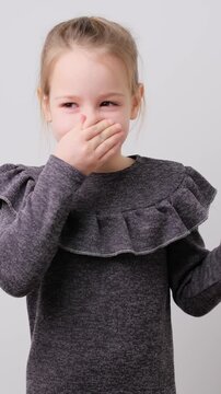 vertical Portrait of preeten girl kid smelling something stinky and disgusting, intolerable smell, holding breath with fingers on nose, hand gesture isolated. Bad smell concept
