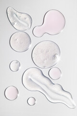Shimmering clear and pink skincare serums and peeling gel swatches on white background