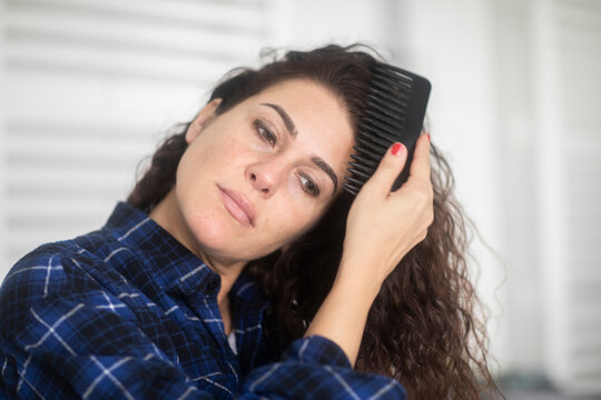 Close-up portrait of a mid adult Woman with long wavy hair standing in bathroom combing her hair