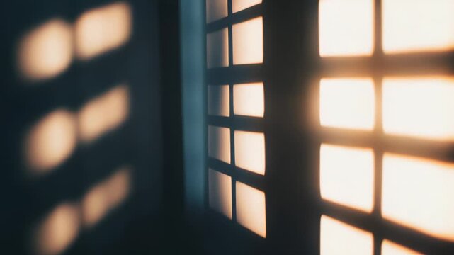 Sunlight beams through a window with a grid pattern, casting rectangular shapes of bright light and soft shadows onto an interior wall, creating a warm and abstract atmosphere