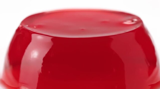 Vibrant Red Gelatin Dessert or Jelly on a White Background. Close-up Macro Shot of Smooth, Glossy Sweet Confectionery.
