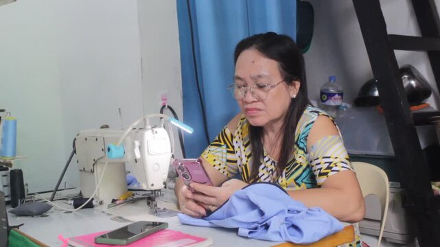  Woman working in the Gown Shop while Chatting a Customers on Mobile Phone thru Communicate a dresses order on the Deadline about Finish Product of Garments