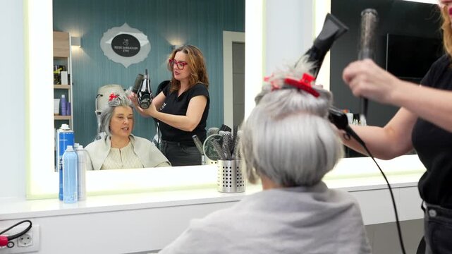 Hairdresser styling senior woman's gray hair with hairdryer