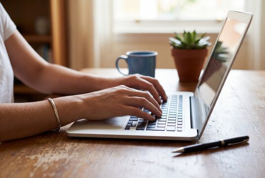 Woman working remotely on laptop computer at wooden desk with coffee mug and succulent plant