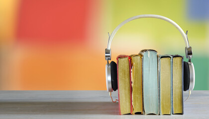 audiobooks concept with  stack of books and headphones, smooth blurry color background.