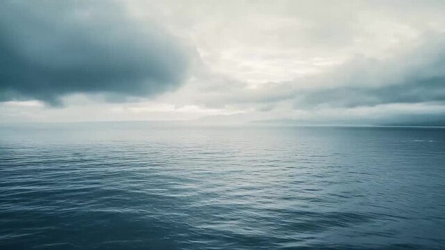 Ocean water stretching to the horizon under a heavily clouded, gray sky, with distant landforms faintly visible, creating a serene and expansive natural scene