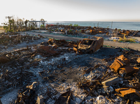 Aerial view of charred remains and ghostly silhouettes of vehicles and structures against the tranquil ocean backdrop at Pacific Palisades Bowl, Pacific Palisades, California, United States.