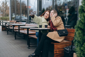 Obraz premium Two young women take a selfie with a camera while enjoying coffee together at an outdoor cafe, sharing a cheerful and friendly moment.