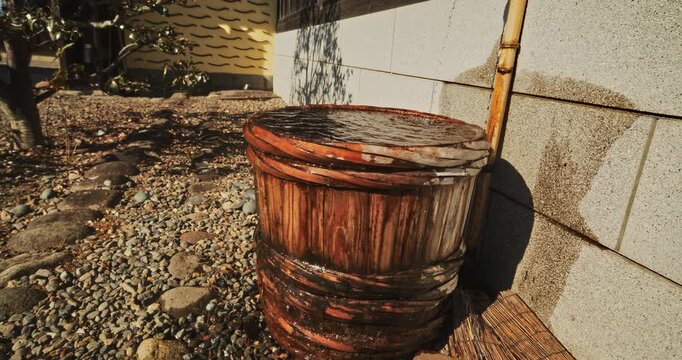 Water coming out of bamboo faucet and falling into overflowing wooden bucket in old Japanese town